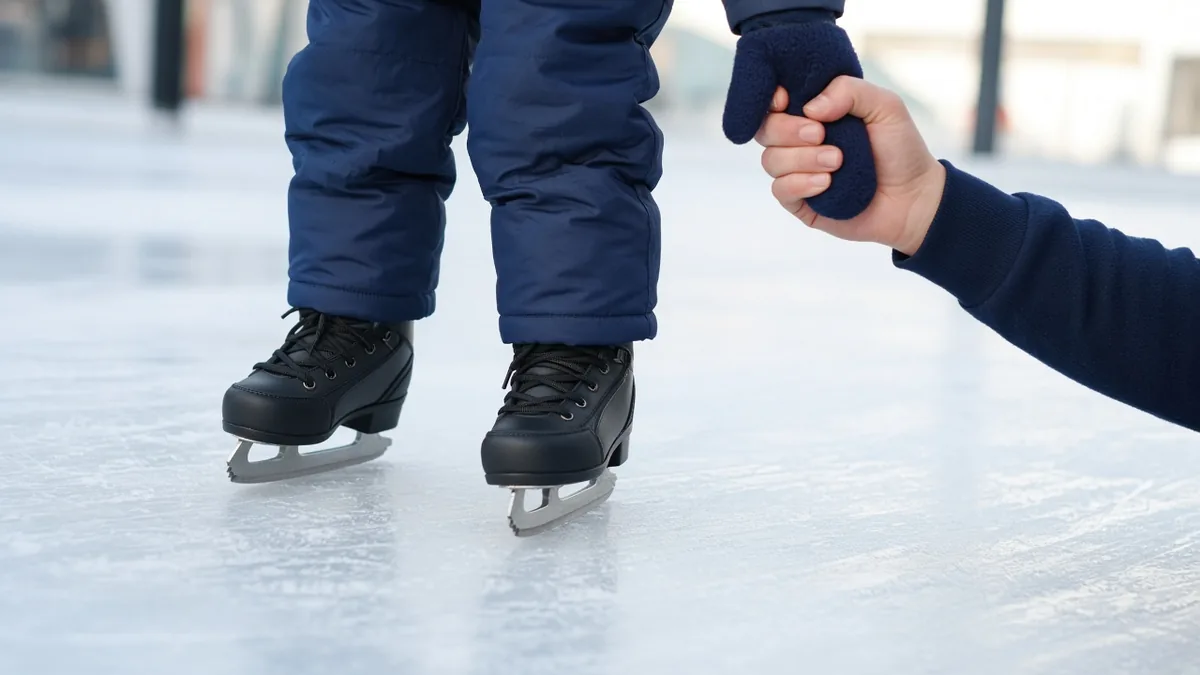 Kind auf Kinder-Schlittschuhen auf der Eisbahn, ein Elternteil hält die Hand – Kinder-Schlittschuhe kaufen